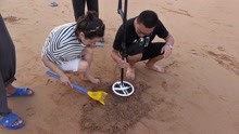 拿着金属探测器在海滩探宝，挖出的东西引一群人围观